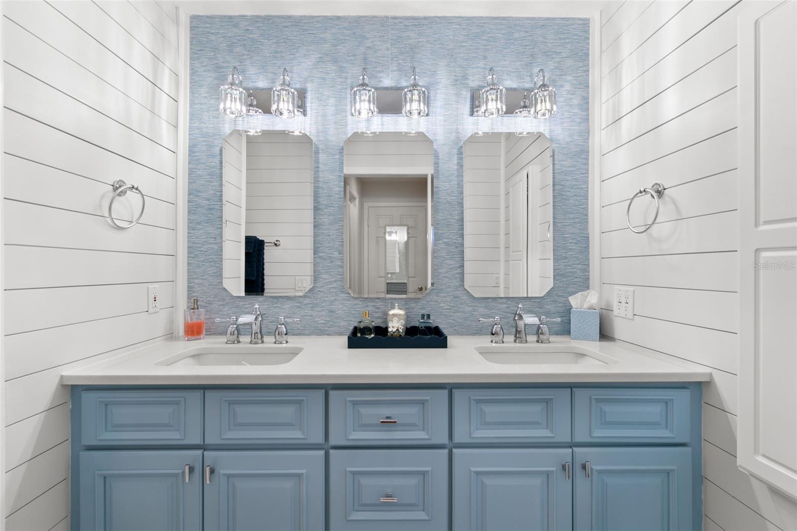 Primary ensuite featuring a double-sink vanity with stone countertop, ample cabinet storage, wall-mounted mirrors, and updated lighting.