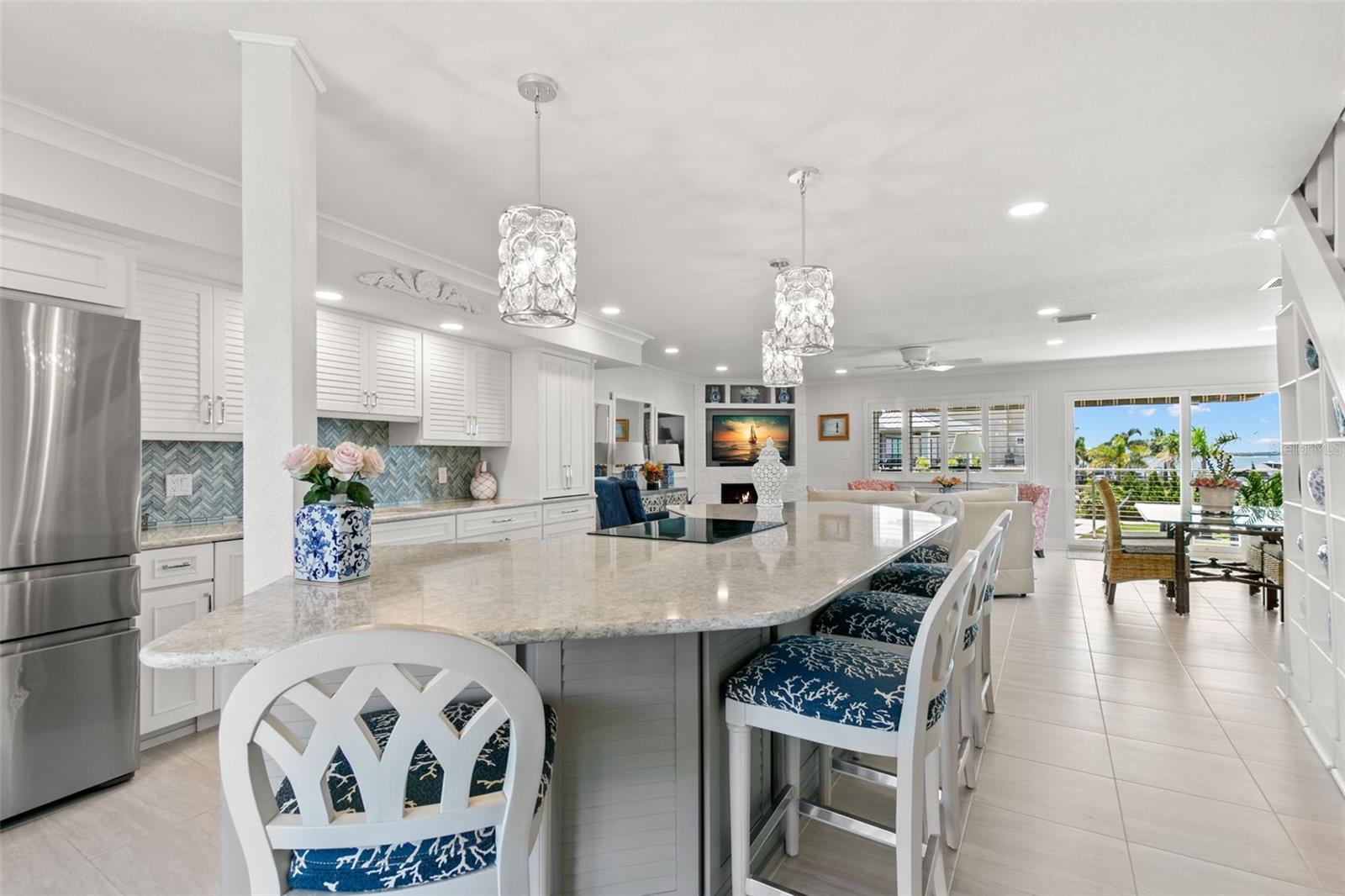 Spacious open kitchen anchored by an oversized stone island with seating, pendant lighting, and clear sightlines into the living area and waterfront beyond.