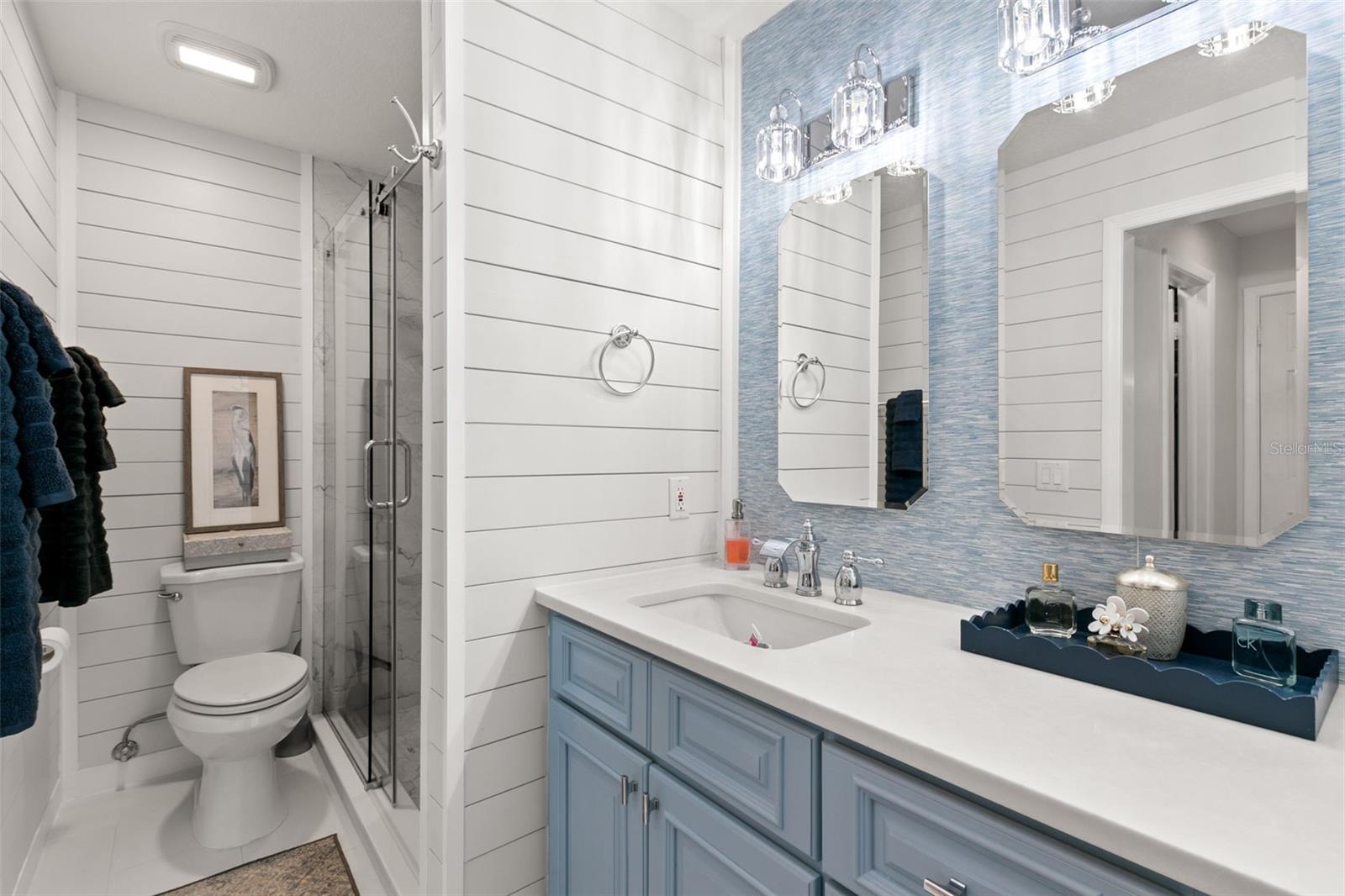 Well-appointed ensuite bath showcasing a dual vanity layout, shiplap wall detailing, and a walk-in shower with glass enclosure.