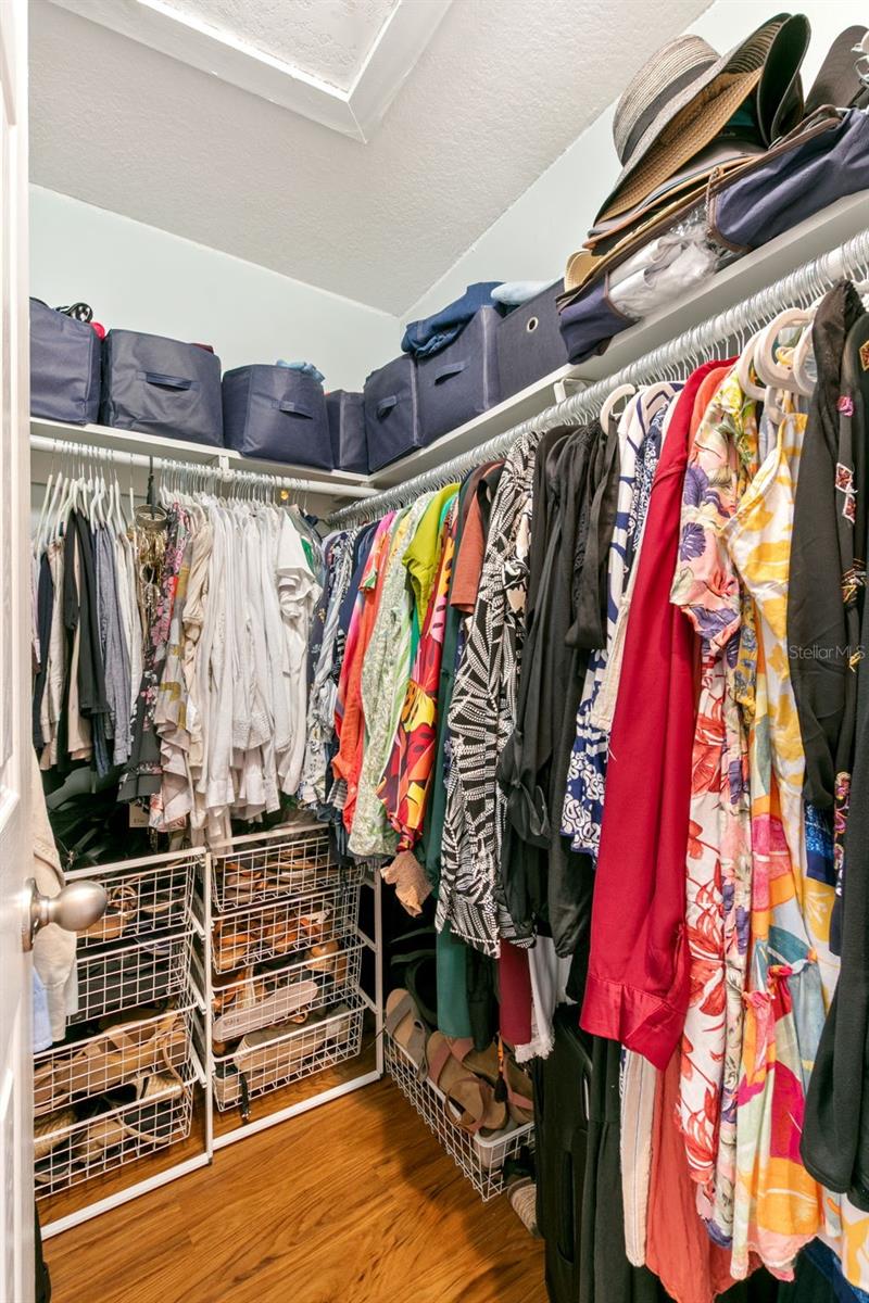 Walk-in primary closet with built-in hanging rods, shelving, and wood flooring, providing ample storage and organization space.