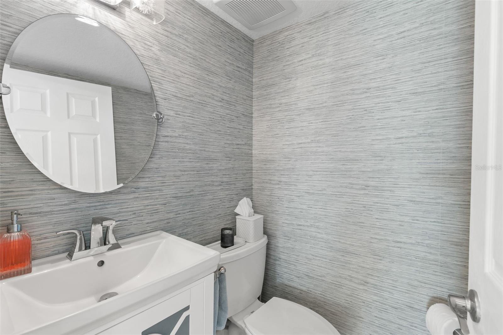 Well-appointed half bath featuring a compact vanity with integrated sink, chrome faucet, round wall mirror, and textured wall finish for a clean, contemporary look.