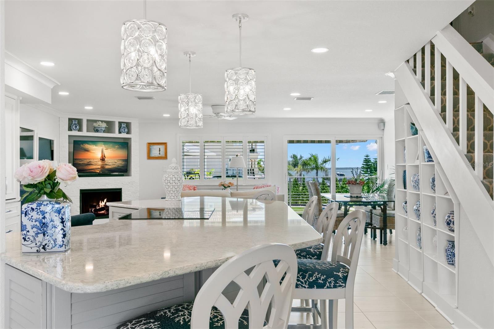 Open-concept layout showcasing the kitchen island, custom fireplace, and dining area, with large windows drawing in natural light and water views.
