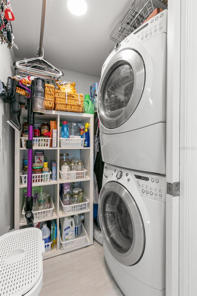 Efficient laundry  featuring a stacked washer and dryer, overhead shelving, and built-in storage for supplies and organization.