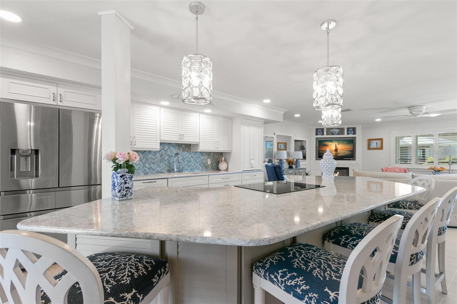 Generous kitchen island with smooth stone counters, integrated cooktop, and abundant seating, framed by custom cabinetry and coastal-inspired finishes.