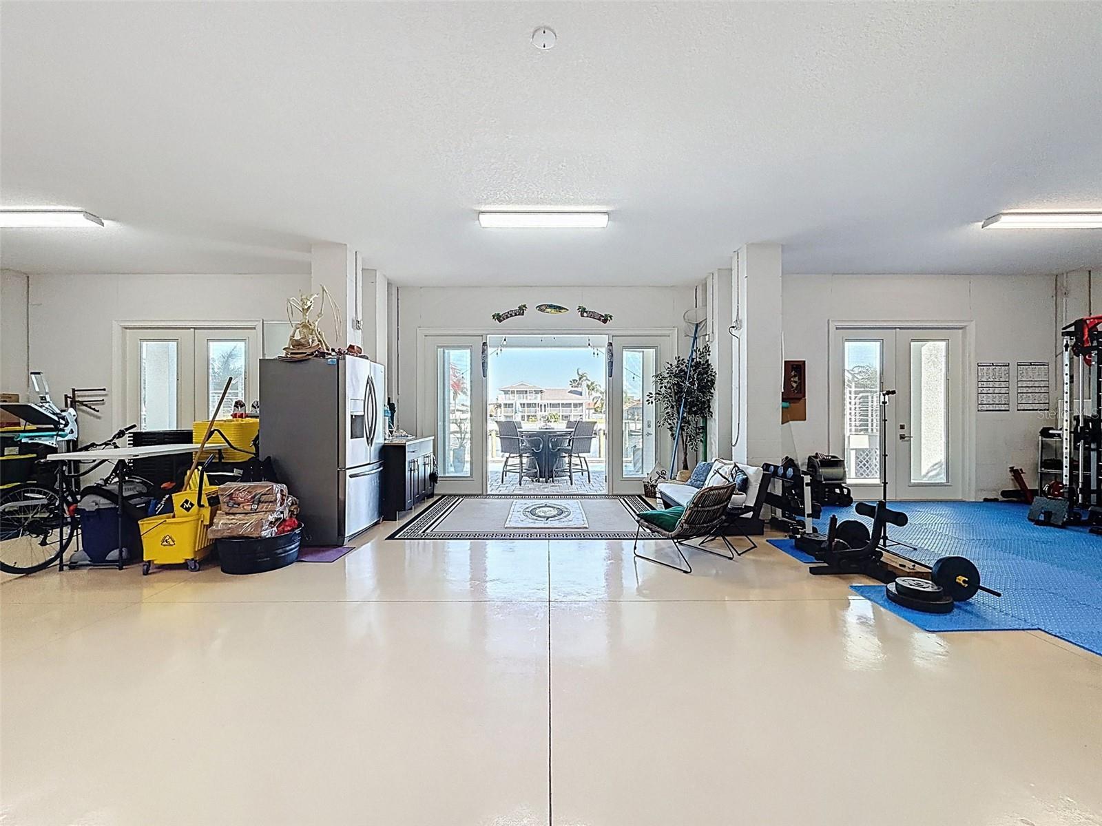 Massive climate-controlled garage level with epoxy flooring, high ceilings, and multiple French doors opening to the pool area