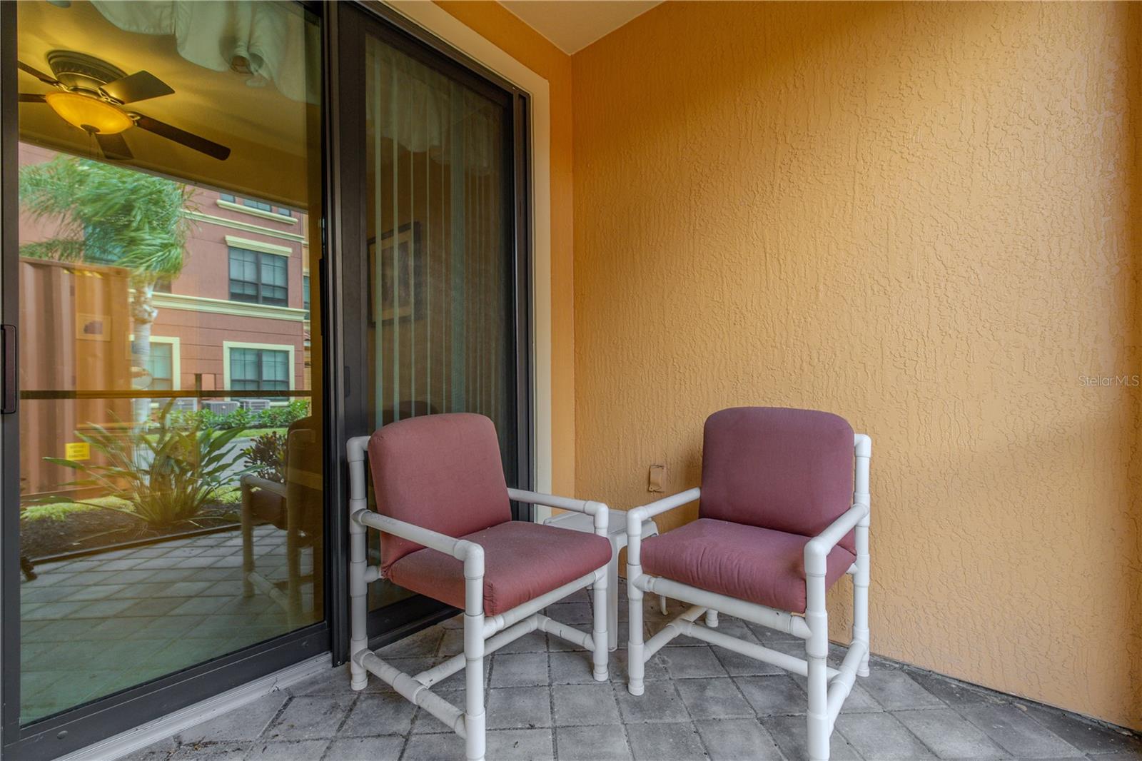 Private screened-in patio with pavered flooring and a cozy seating nook, offering a quiet spot to relax and enjoy fresh air with views of the landscaped courtyard beyond.