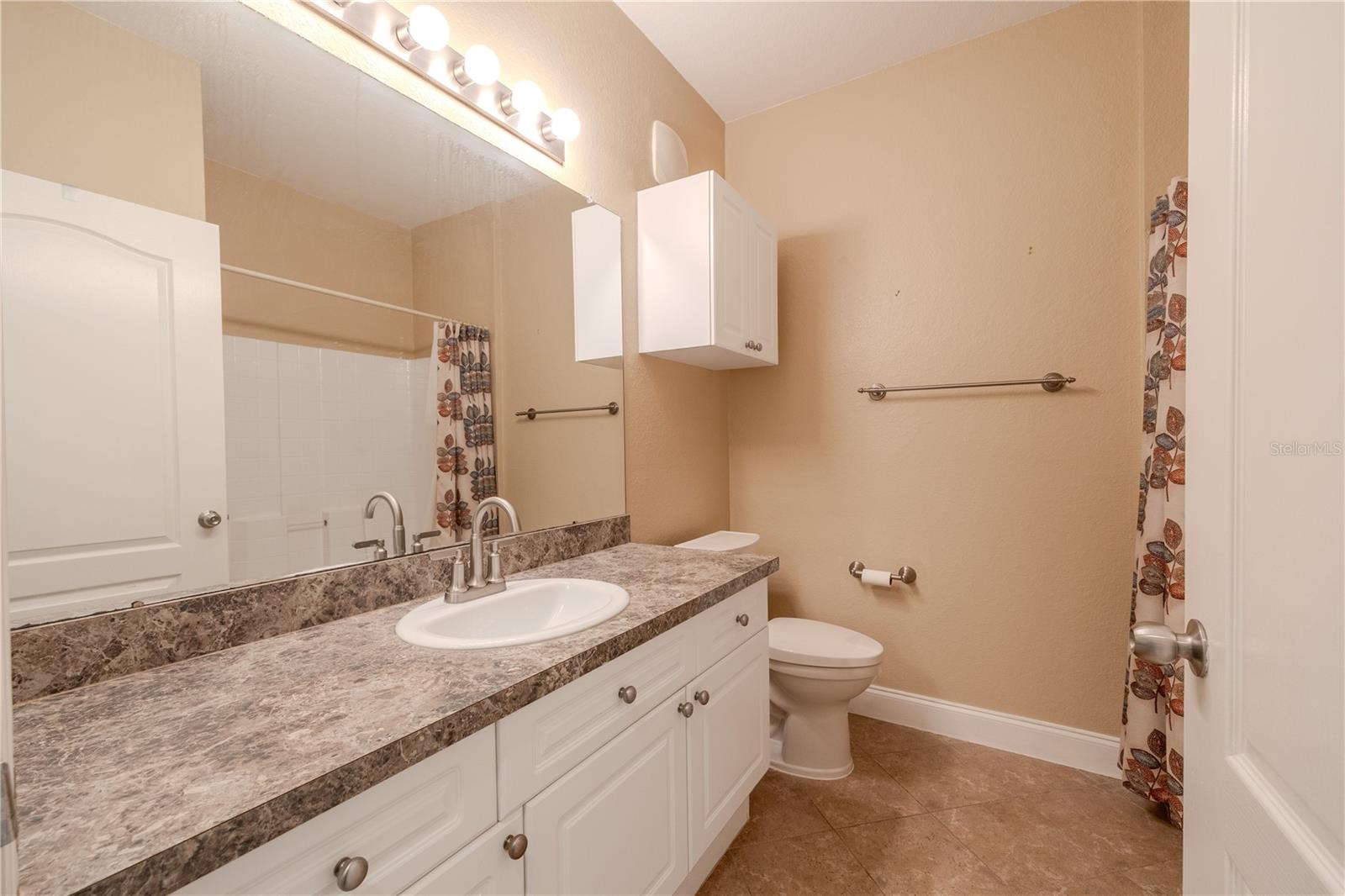 2nd bathroom features a single-sink vanity with a stone-look countertop, white cabinetry, and an oversized mirror with above mirror lighting.