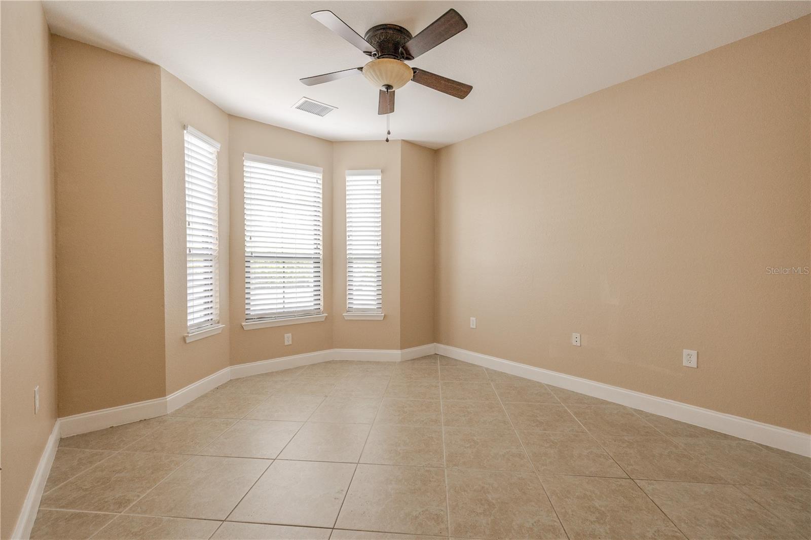 Bedroom 2 includes multiple windows that bring in natural light, along with tile flooring and a ceiling fan that adds comfort and year-round airflow.