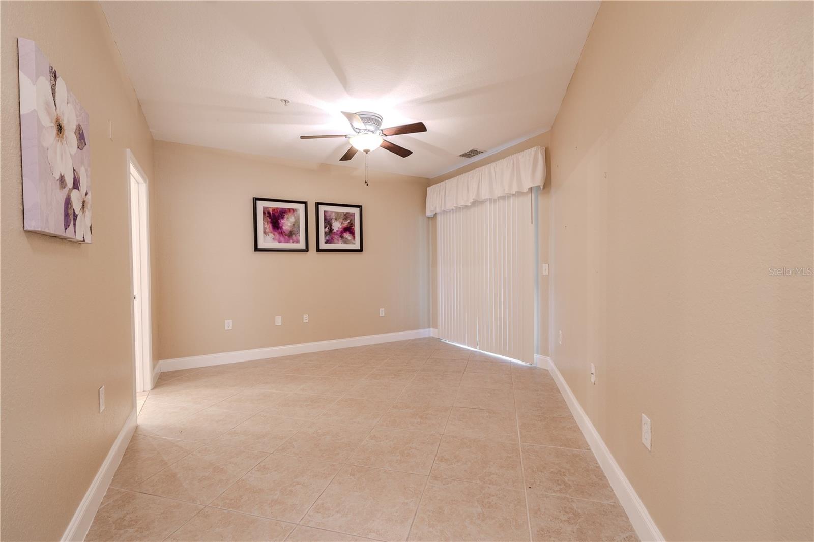 Spacious primary bedroom features tile flooring, neutral walls, and a ceiling fan with light, creating a calm and comfortable retreat.