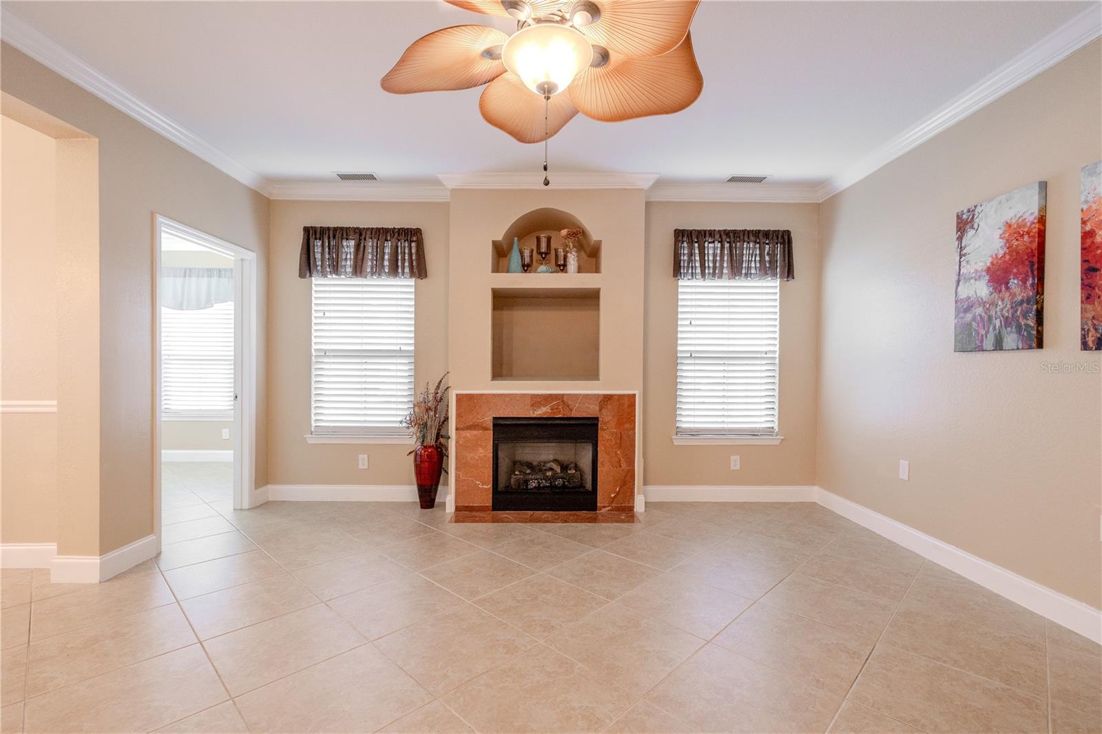 A tiled gas fireplace anchors the living space, framed by custom built-in niches that add architectural interest and display space. Two large windows bring in natural light, enhancing the room’s warm, inviting atmosphere.
