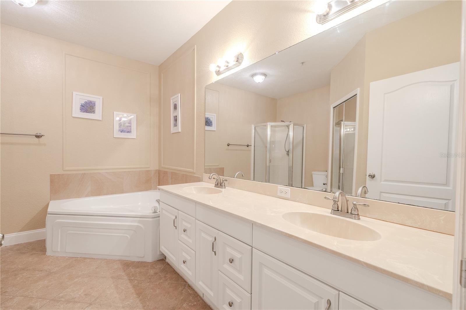 Spacious primary bath with dual-sink vanity, expansive mirror, and neutral tile flooring.