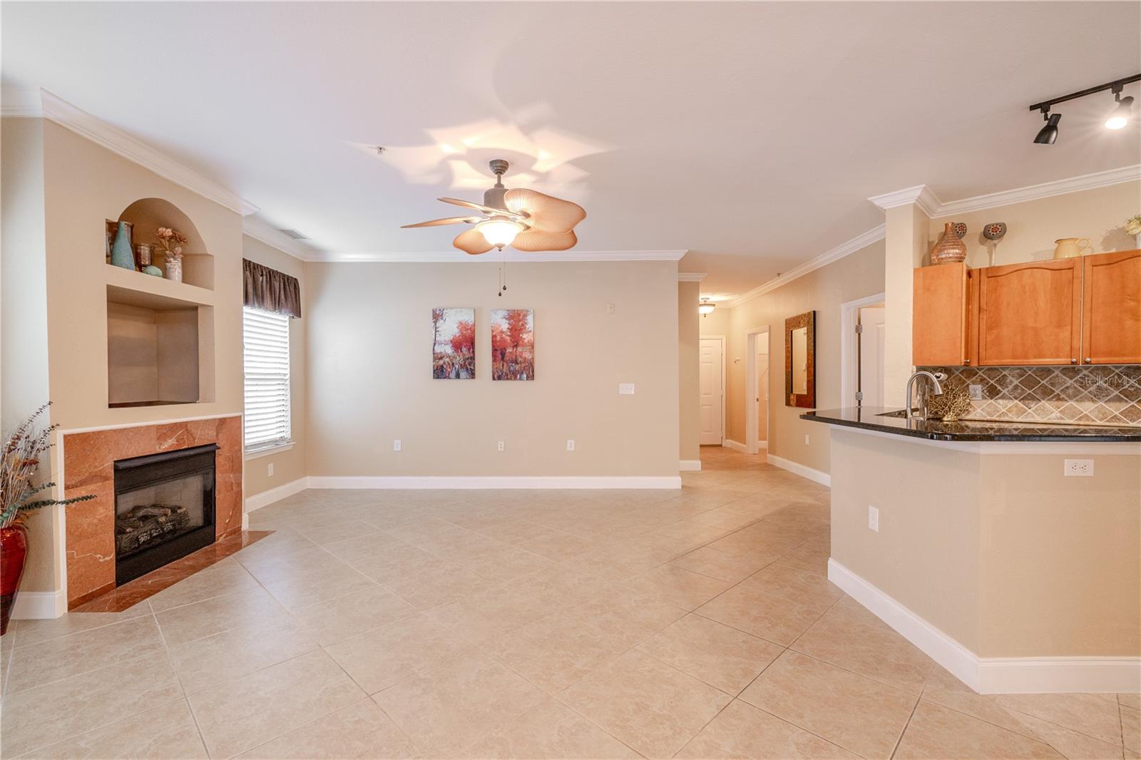 Spacious living room features a tiled fireplace with built-in niches, neutral tile flooring, crown molding, and an open connection to the kitchen and dining areas.