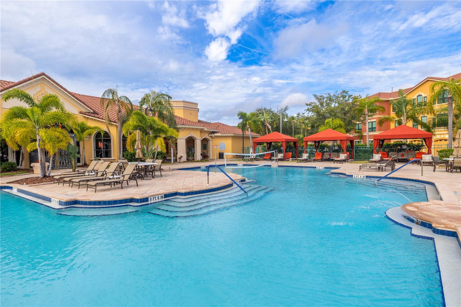 The resort-style heated clubhouse pool features a zero-entry sun shelf, a palm-lined deck with lounge seating, and private cabanas, all framed by beautiful Mediterranean architecture for a true vacation-at-home feel.