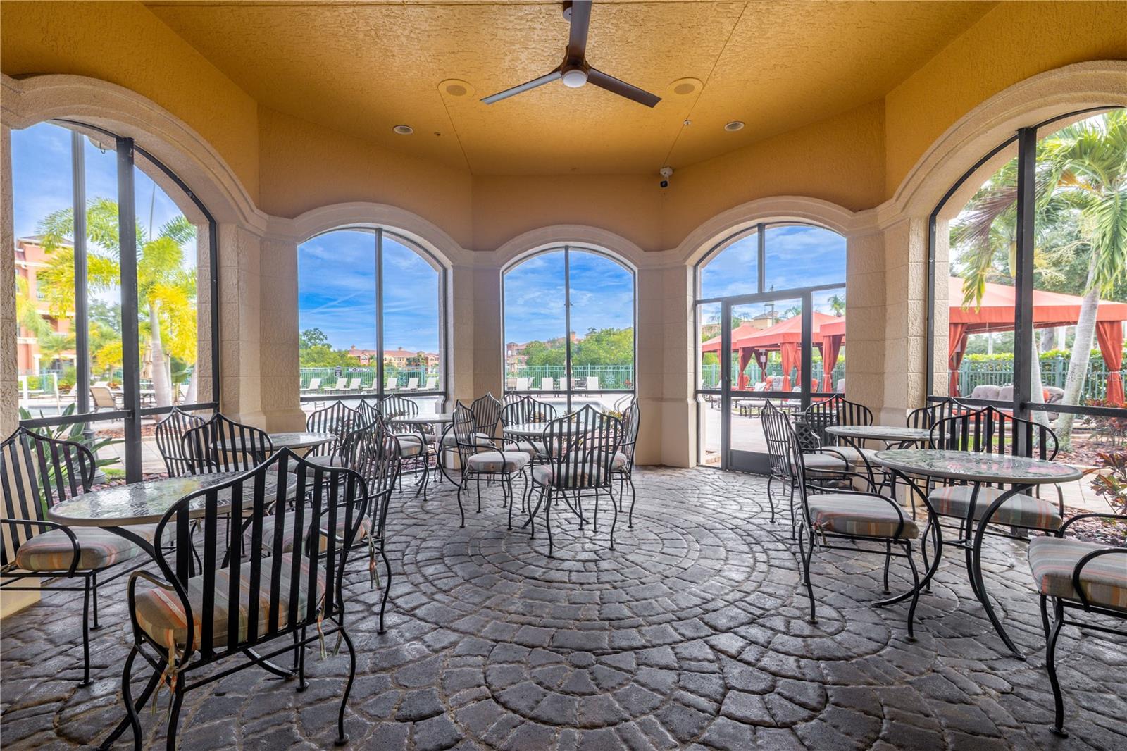 The covered poolside pavilion features café-style seating, a ceiling fan, and charming arched openings—ideal for unwinding in the shade while taking in views of the resort-style pool and cabanas.