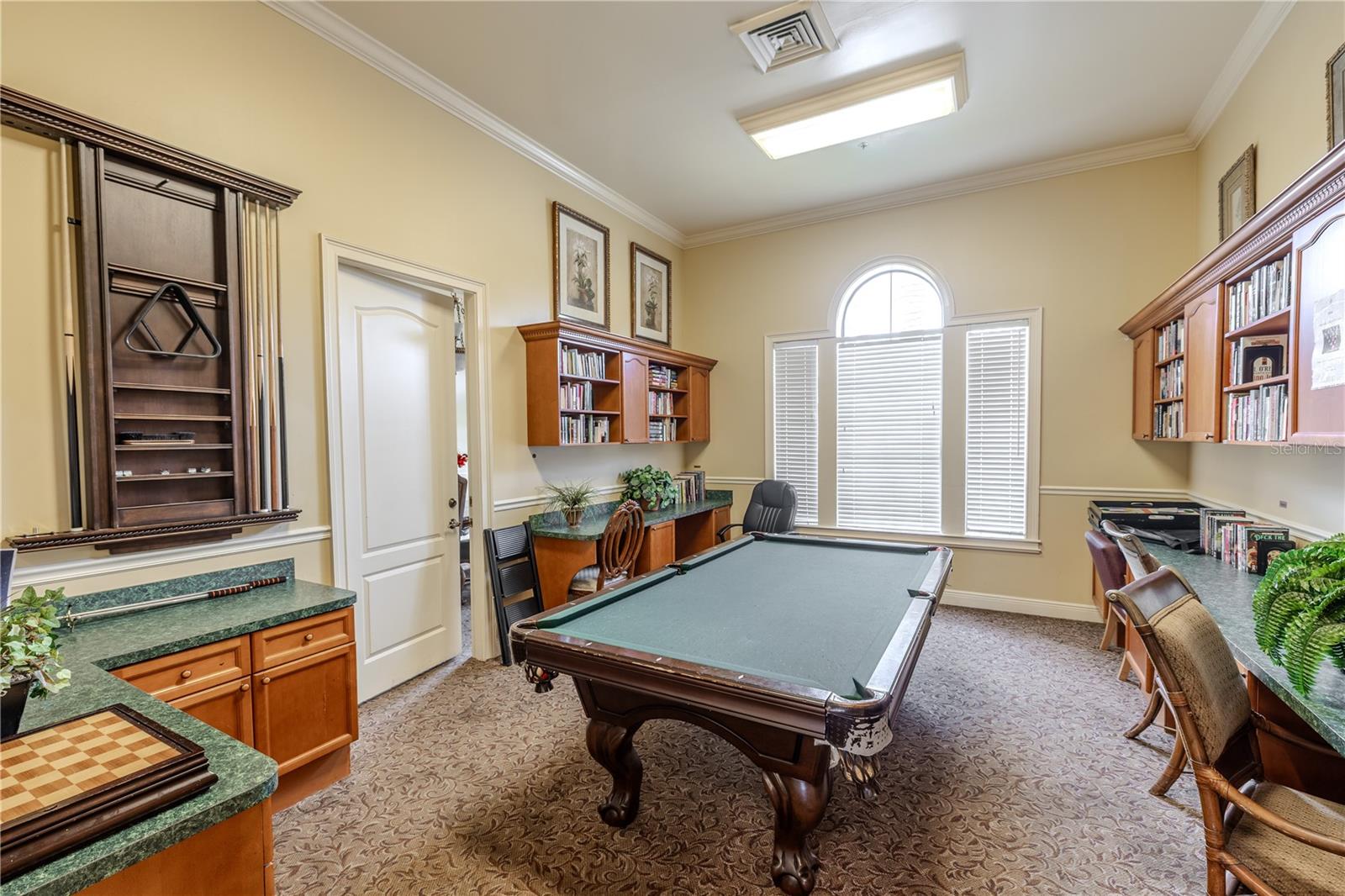 The clubhouse game and lounge room includes a billiards table, built-in counters and cabinetry, and a sunlit arched window—ideal for gathering with neighbors, playing a round of pool, or simply unwinding.