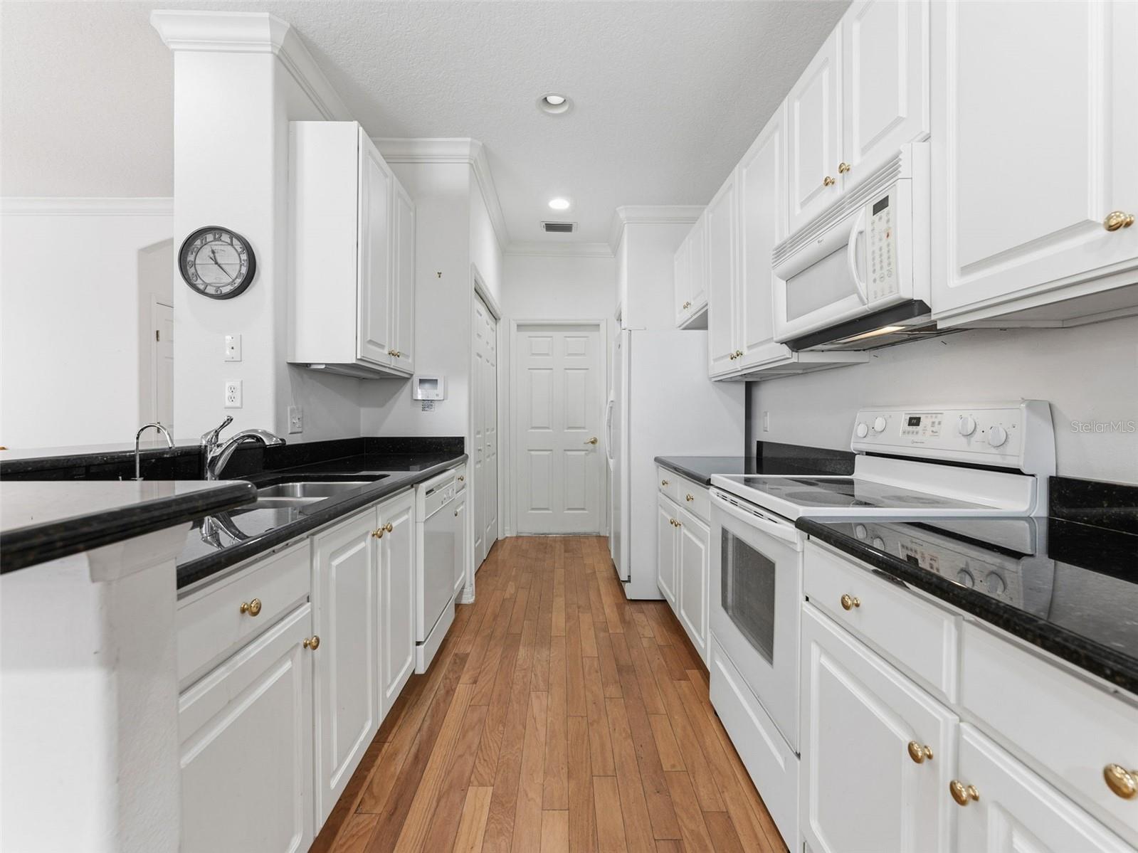 Step saver galley kitchen with laundry closet, pantry and entry to garage; gleaming white cabinets and granite counters