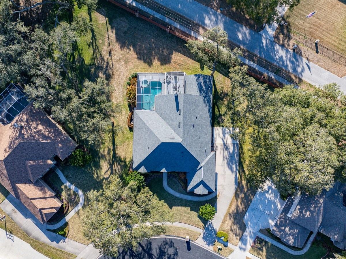 Aerial view highlights a spacious corner lot, screened pool enclosure, and wide driveway amid mature trees!