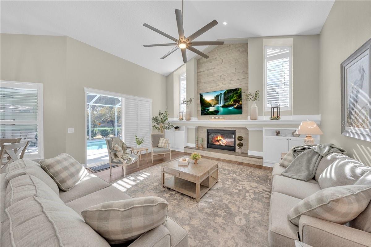 Vaulted family room showcases a dramatic stone fireplace, built-ins, and oversized windows for abundant light!