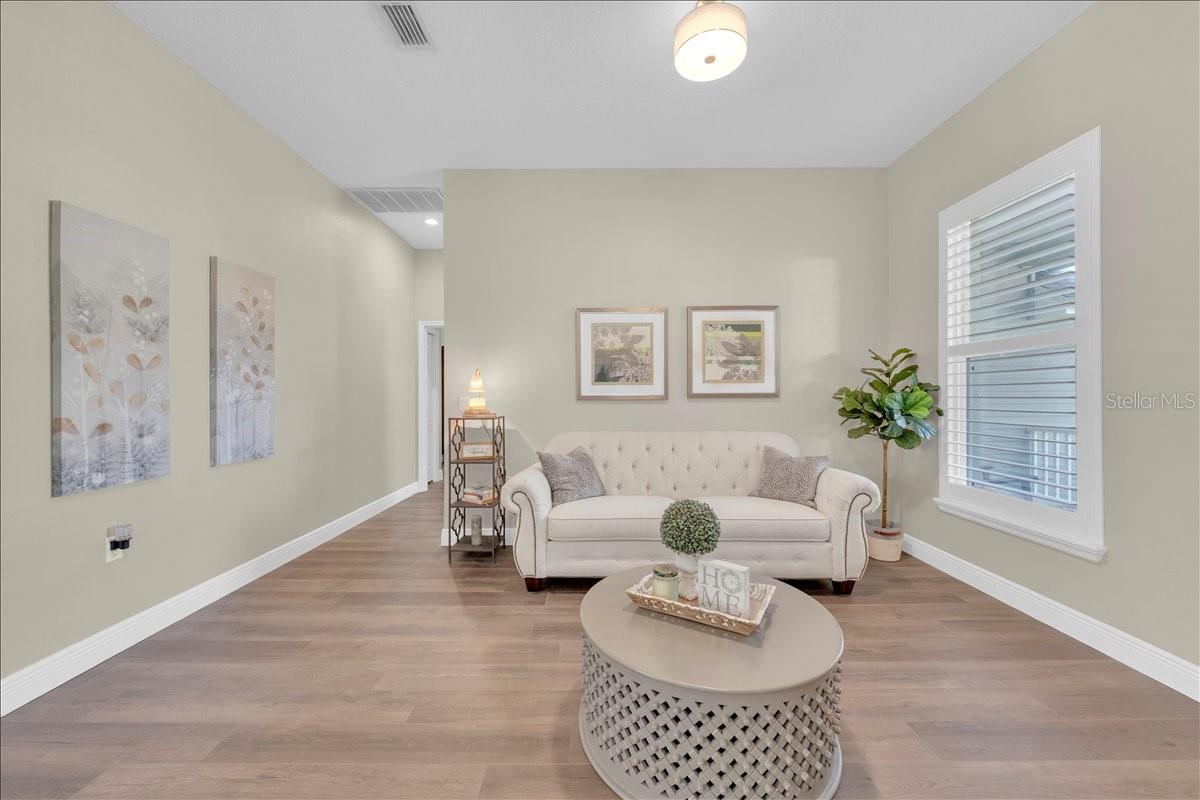 Inviting living room with wide-plank floors, tall ceilings, and a large window with plantation shutters!