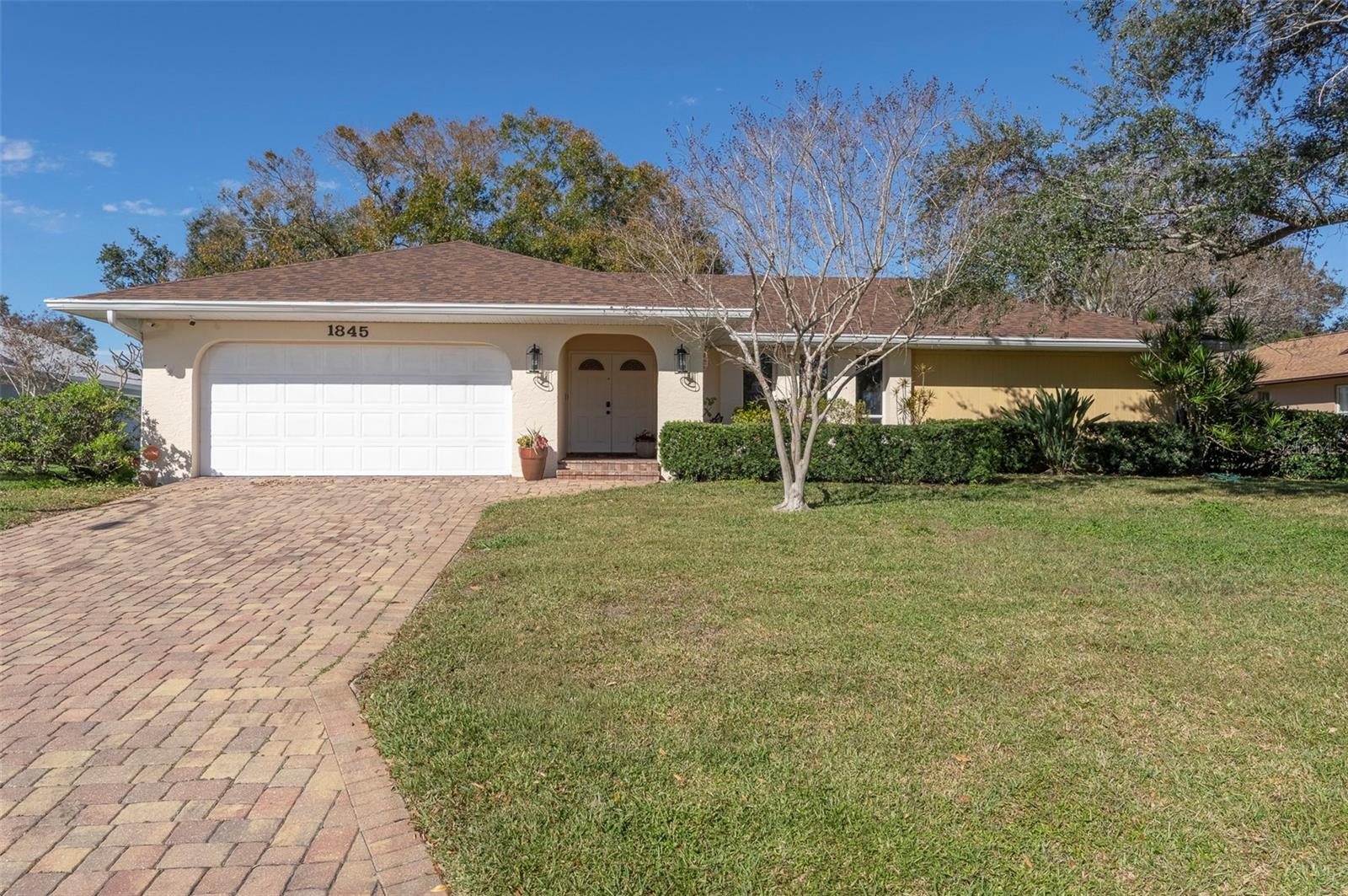 EXTEROR FRONT WITH A PAVER DRIVEWAY AND LUSH LANDSCAPING.