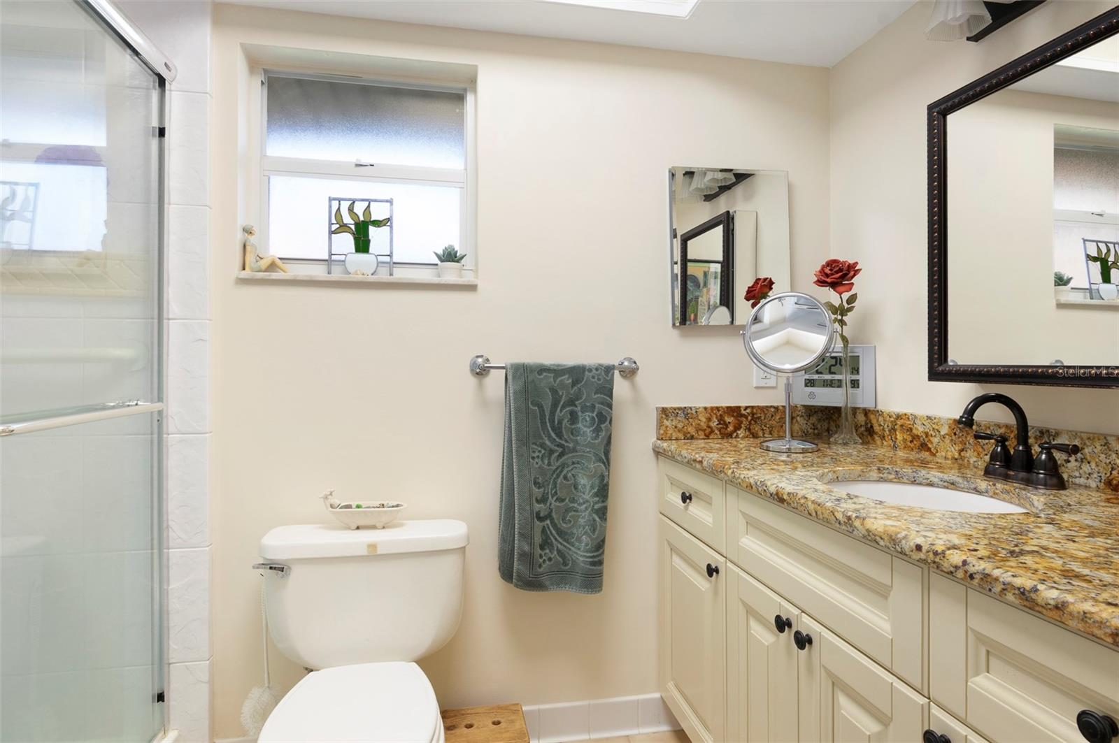 PRIMARY BATH WITH WALK IN SHOWER AND GRANITE COUNTERTOPS.