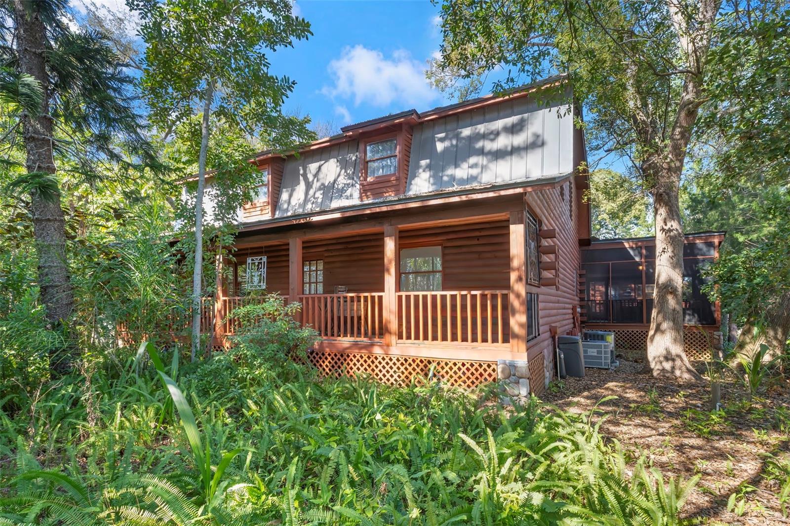 Timeless log-style architecture set in a private, wooded environment with inviting covered porch spaces and enduring character. Front elevation showcasing classic log-style construction, a covered porch, and a peaceful woodland setting surrounded by mature trees and native landscaping.