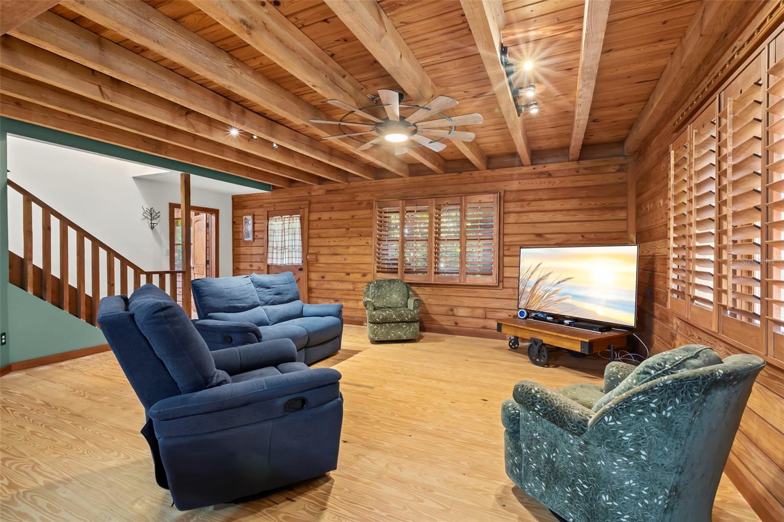 Living room finished in natural pine with exposed wood beam ceilings, wide plank flooring, and a sculptural ceiling fan designed to complement the home’s rustic architecture.