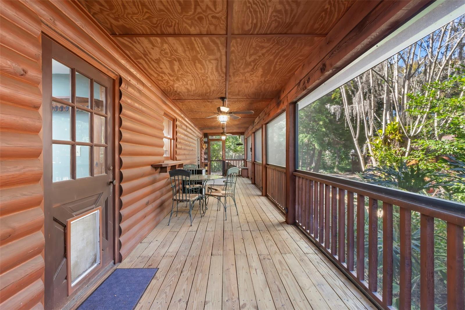 This expansive screened porch extends the living space outdoors, offering a peaceful setting beneath a wood-paneled ceiling with ceiling fans for added comfort. Surrounded by mature trees, it’s an ideal spot for morning coffee, afternoon reading, or relaxed gatherings at sunset.