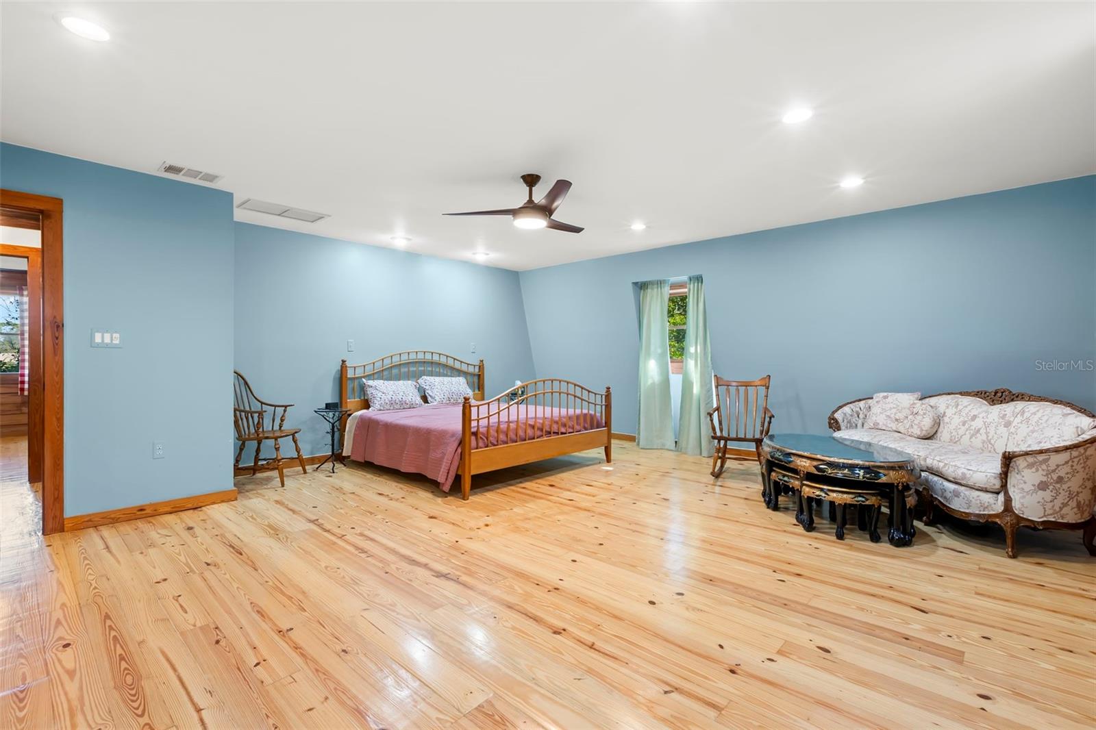 An impressively scaled primary bedroom offering wide-plank wood flooring, recessed lighting, and a modern ceiling fan, with generous proportions that comfortably accommodate both sleeping and sitting areas.