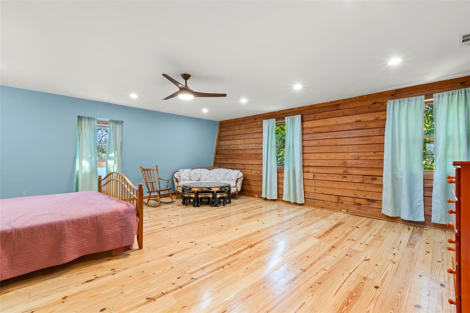 Warm wood accents, multiple windows, and continuous wood flooring give the primary bedroom an open, balanced feel, while the expansive footprint allows for flexible layout options rarely found in a single space.