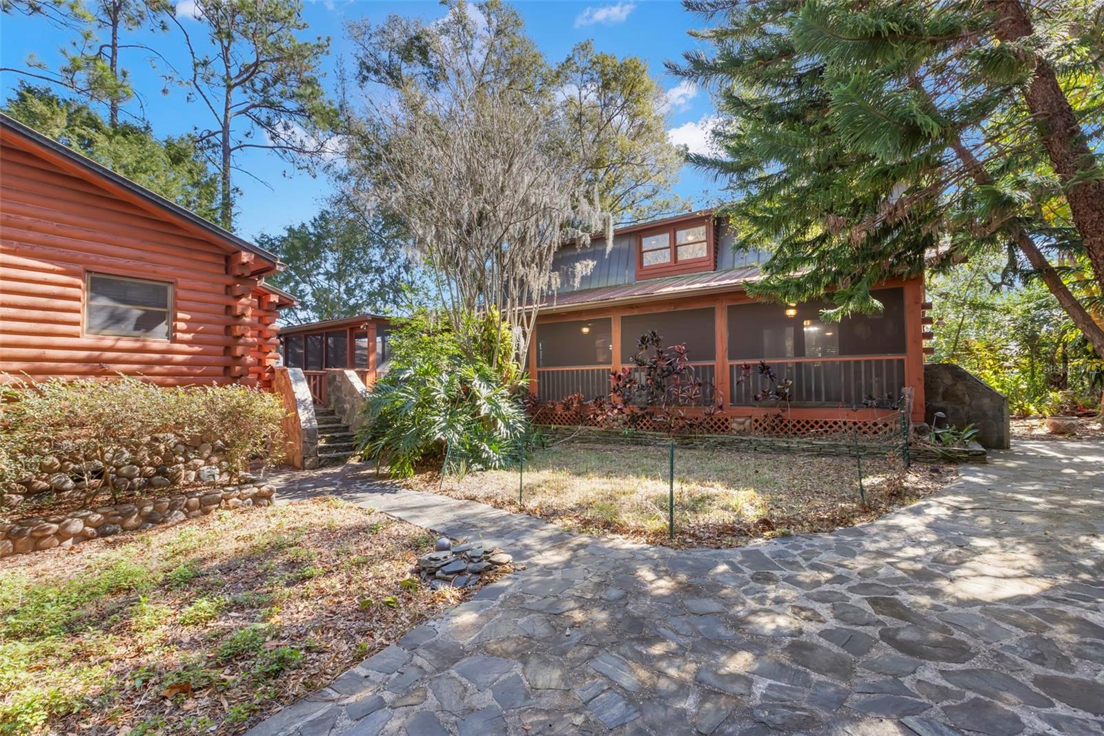 Private Retreat with Storybook Charm!  Tucked beyond the main residence, this detached guest house feels like a destination all its own. Wrapped in warm log-style siding and surrounded by mature trees, it offers a sense of privacy and quiet that invites lingering stays. Stone pathways lead the way, while a screened porch stretches across the front, creating a natural gathering spot for morning coffee, evening conversations, or simply taking in the peaceful setting. Whether used for guests, extended family, or a creative hideaway, this separate living space adds flexibility, charm, and a rare layer of versatility to the property.