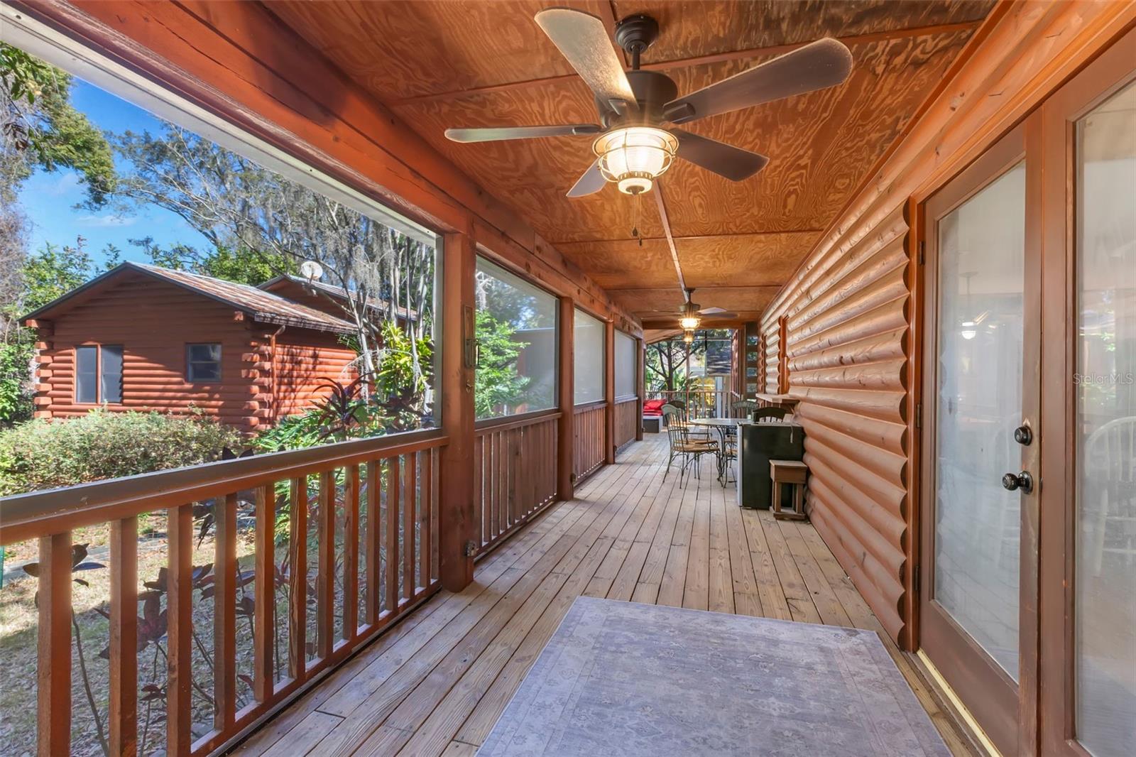 A generous screened-in back porch designed for year-round enjoyment, wrapped in warm wood finishes and framed by tranquil wooded views. Ceiling fans and overhead lighting create a comfortable retreat for lounging, dining, or quiet evenings surrounded by nature.