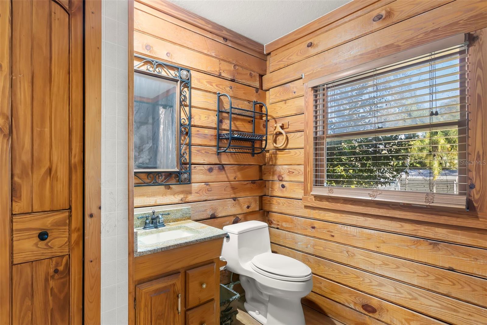 Rustic wood plank walls with exposed log ends surround a thoughtfully updated guest house bathroom, blending cabin character with modern finishes.