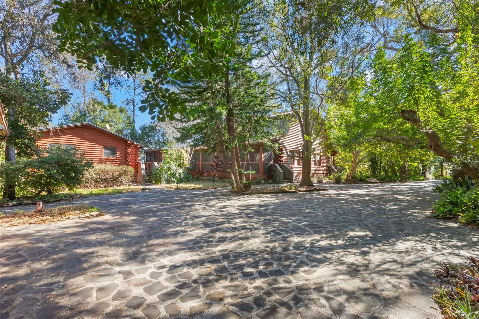 A private, tree-canopied setting where the main residence and detached guest house are thoughtfully arranged around an expansive stone-paved driveway, creating a sense of arrival, separation, and quiet retreat. The natural materials, mature landscaping, and generous layout work together to deliver a property that feels both grounded and intentionally designed.