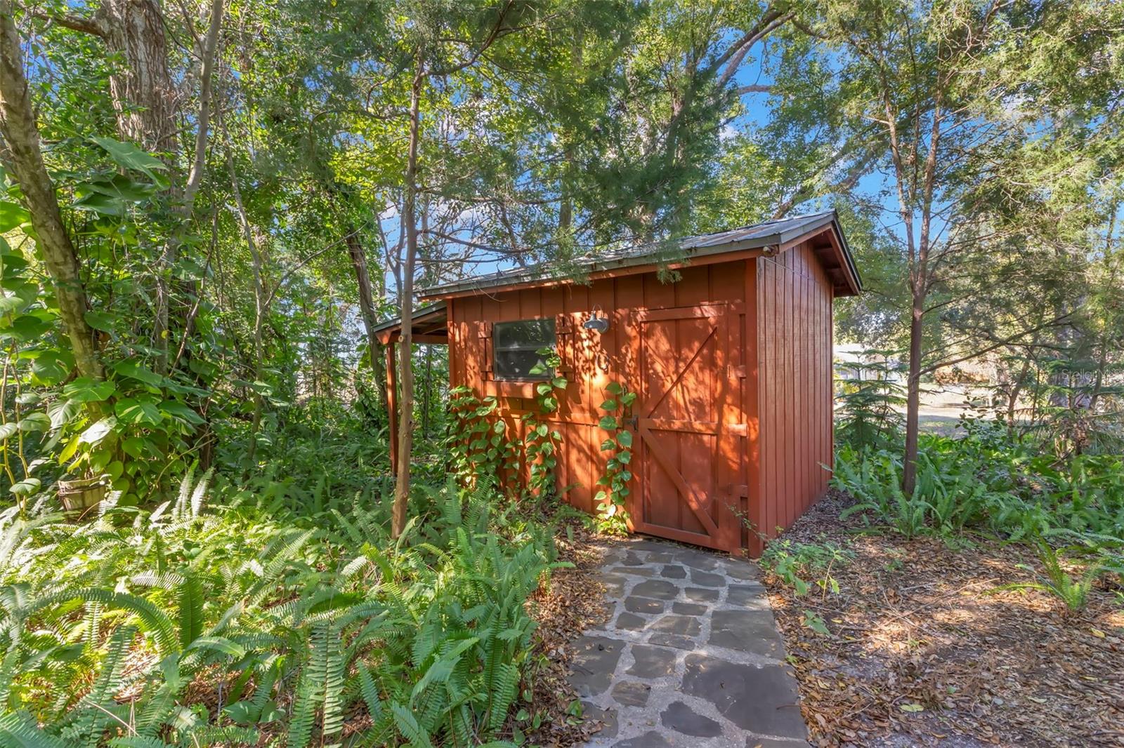 Along a stone path and surrounded by mature greenery, this thoughtfully built wood shed features a solid roof and finished floor, blending function with rustic charm. Its natural setting and handcrafted feel make it as visually appealing as it is practical—ideal for garden storage, tools, or hobby use without disrupting the peaceful landscape.