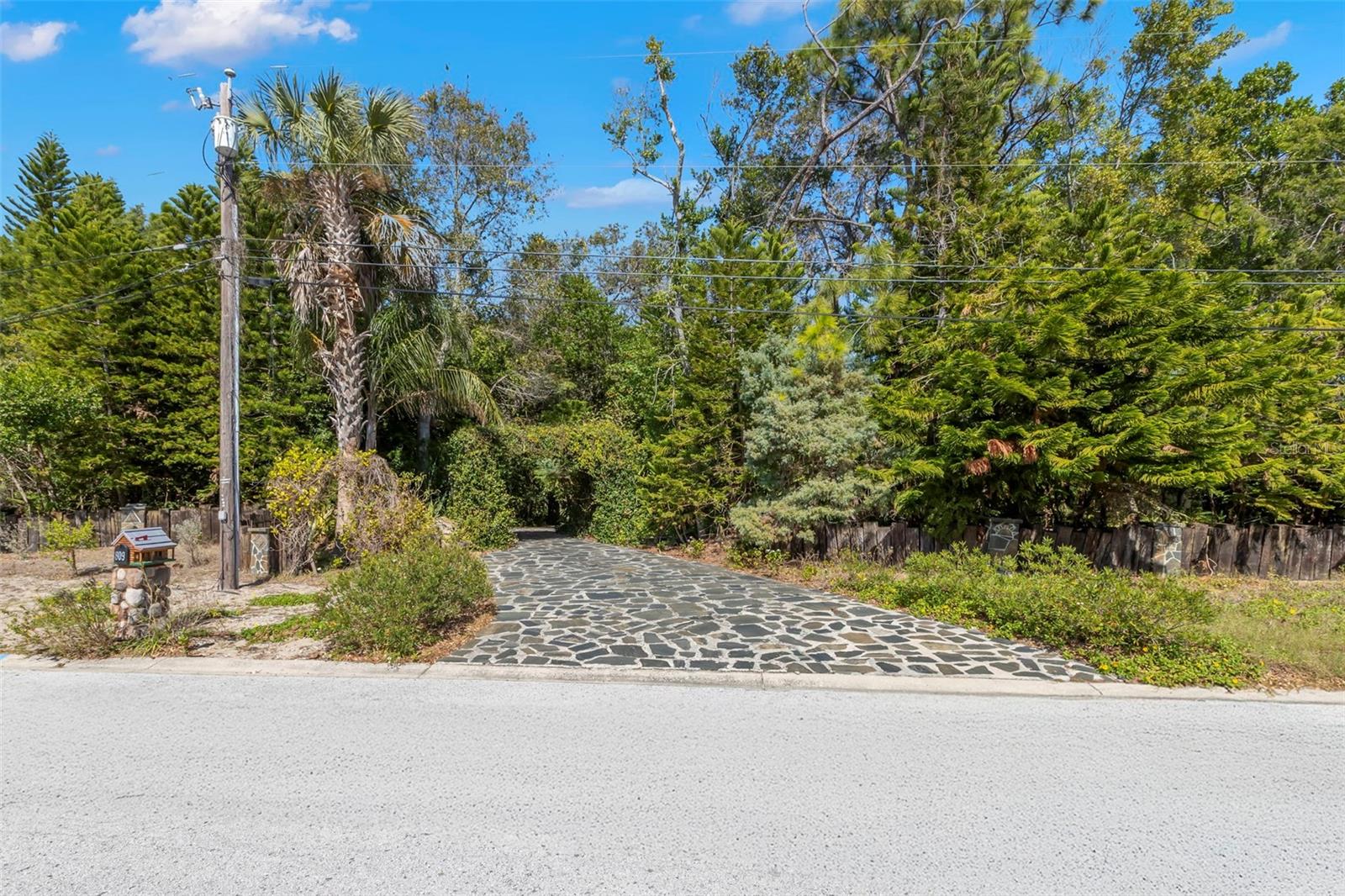 A striking stone-paved drive creates a private, welcoming entrance to the property, framed by mature trees and lush greenery that set the tone for the secluded, compound-like setting beyond.