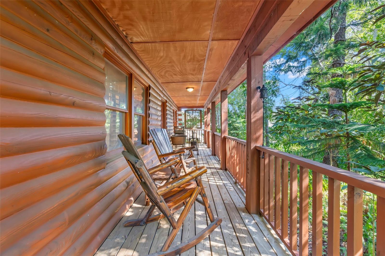The deep covered outdoor space  on the front porch features tranquil views into the surrounding trees
