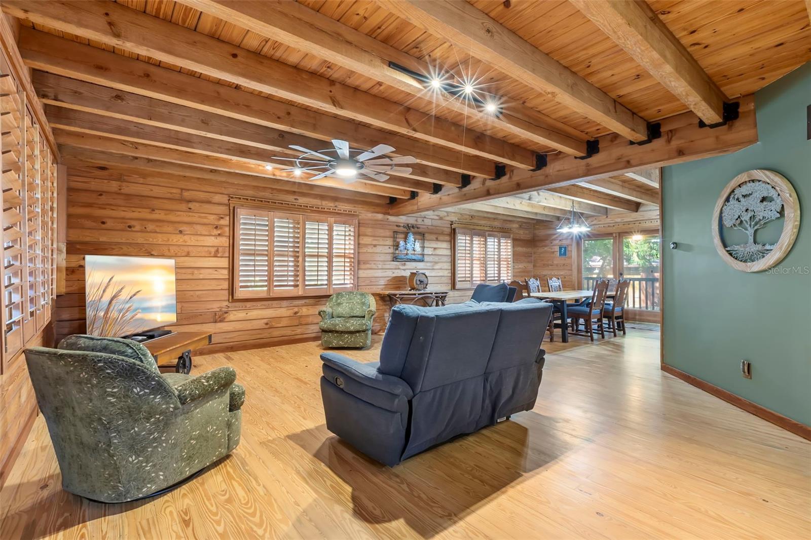 The living area offers generous scale and an open connection to adjacent spaces, with custom wood shutters, layered lighting, and exposed beams that reinforce the home’s craftsmanship.