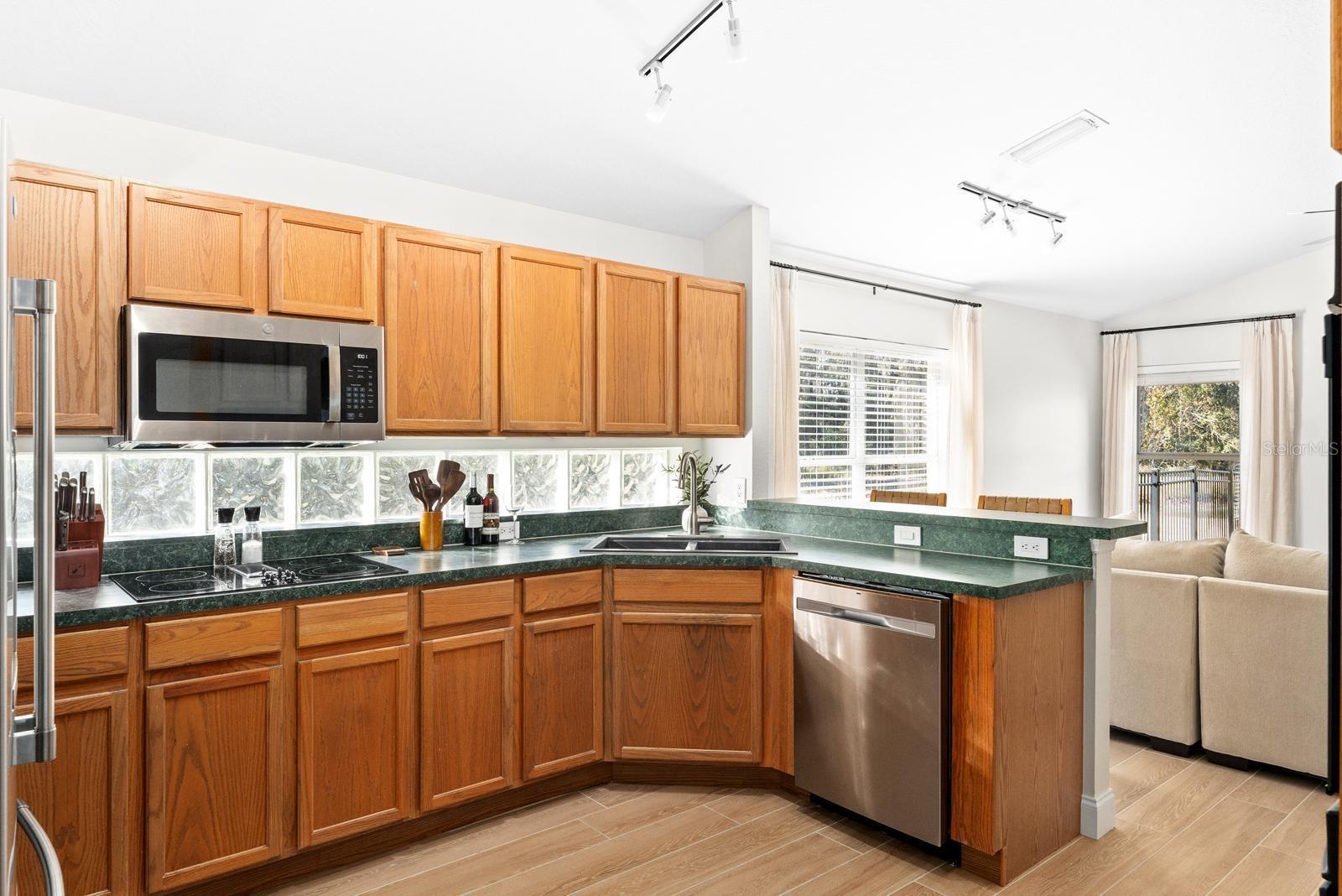 The kitchen is large and features a lot of cabinet space, a double oven, a cooktop, glass windows instead of backsplash, solid wood cabinets, and a counter for a couple of stools.