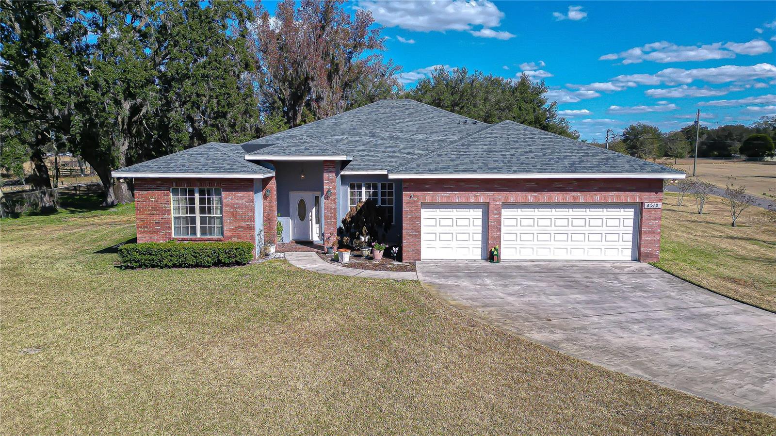 Classic brick exterior with 2025 new roof, covered entry, wide driveway, and expansive front lawn under mature trees on 1.26 acres!