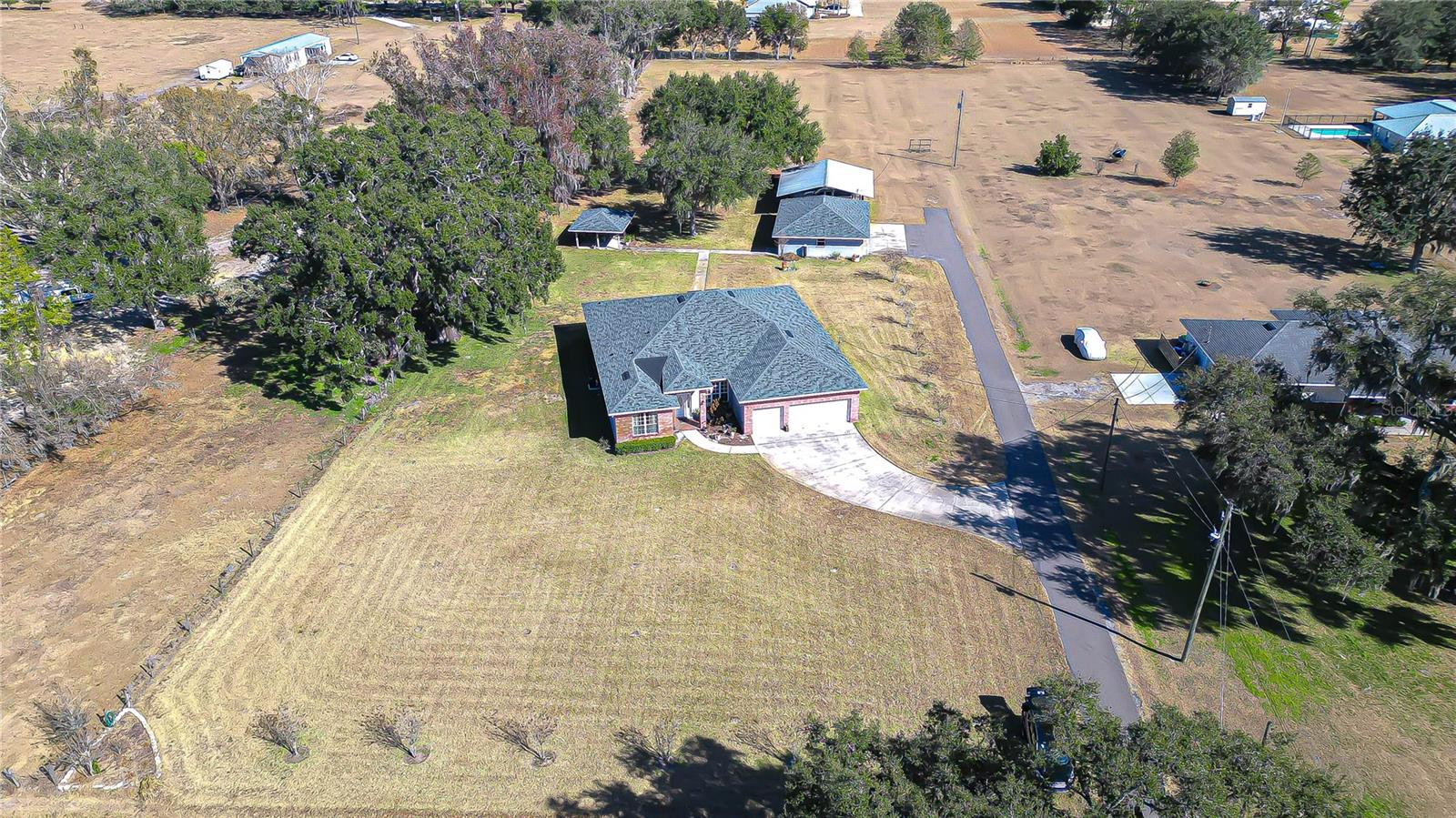 Aerial view highlights long driveway, expansive yard, and detached outbuildings surrounded by mature trees!