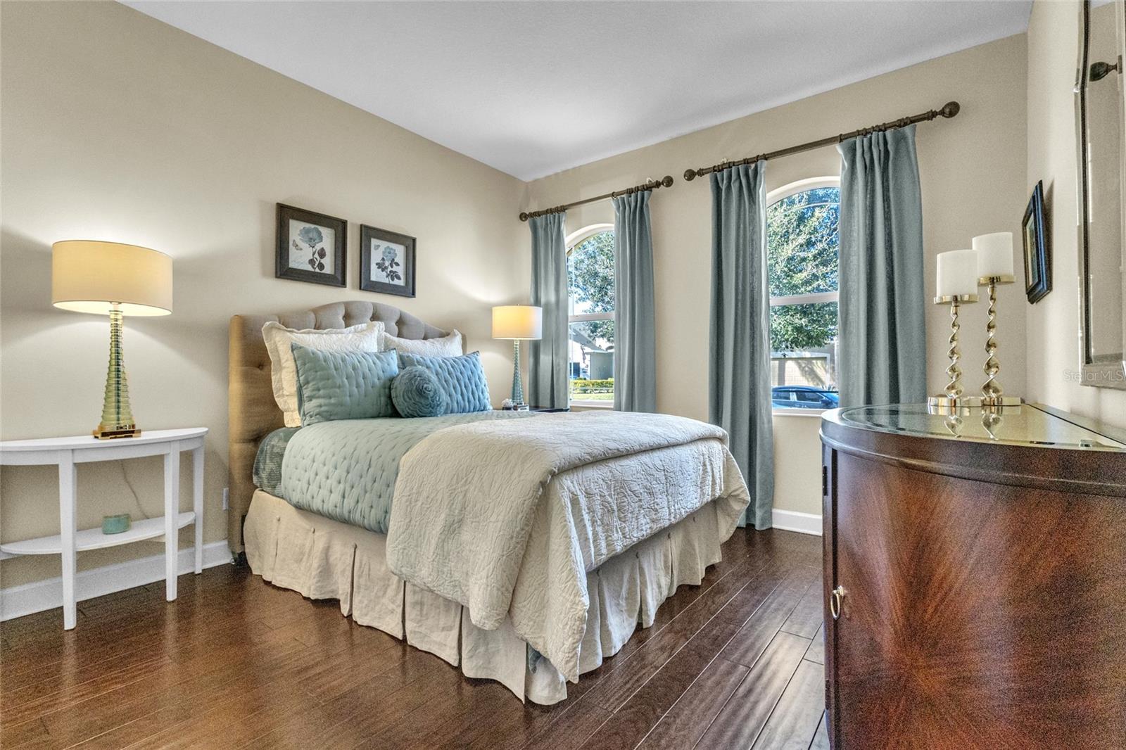 Inviting 2nd bedroom with double arched windows and hardwood flooring.