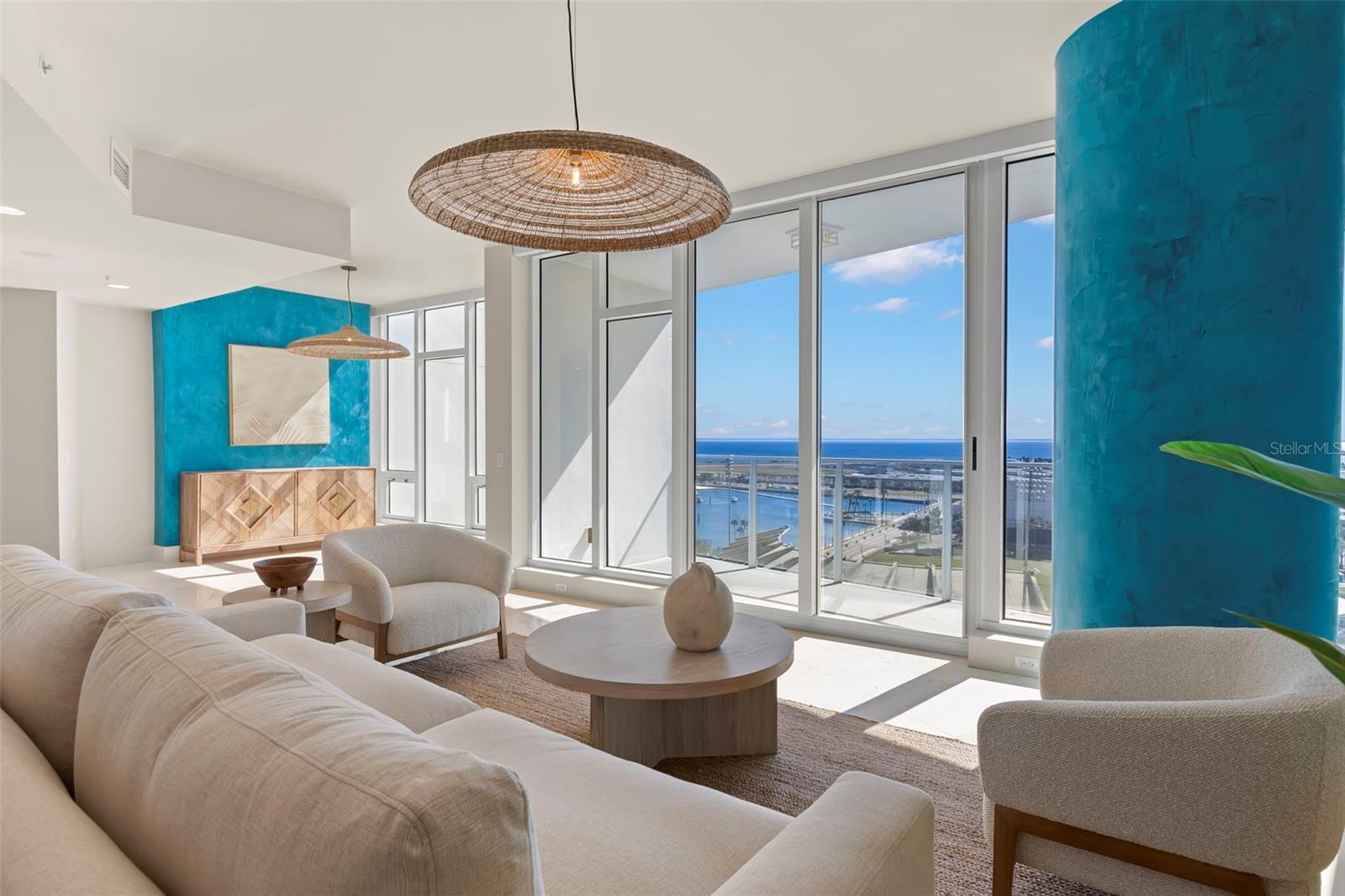 Architecturally striking living room featuring expansive glass walls and bespoke Marmorino plaster accent wall and column in soft coastal blue hues