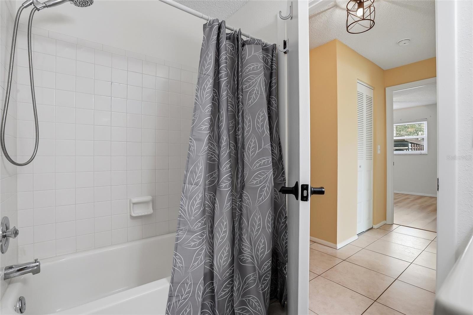 Bright tub/shower with classic tile surround and handheld showerhead.