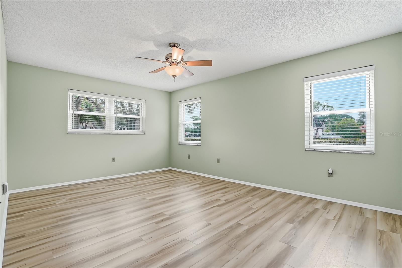 Light-filled primary bedroom with corner windows and ceiling fan.