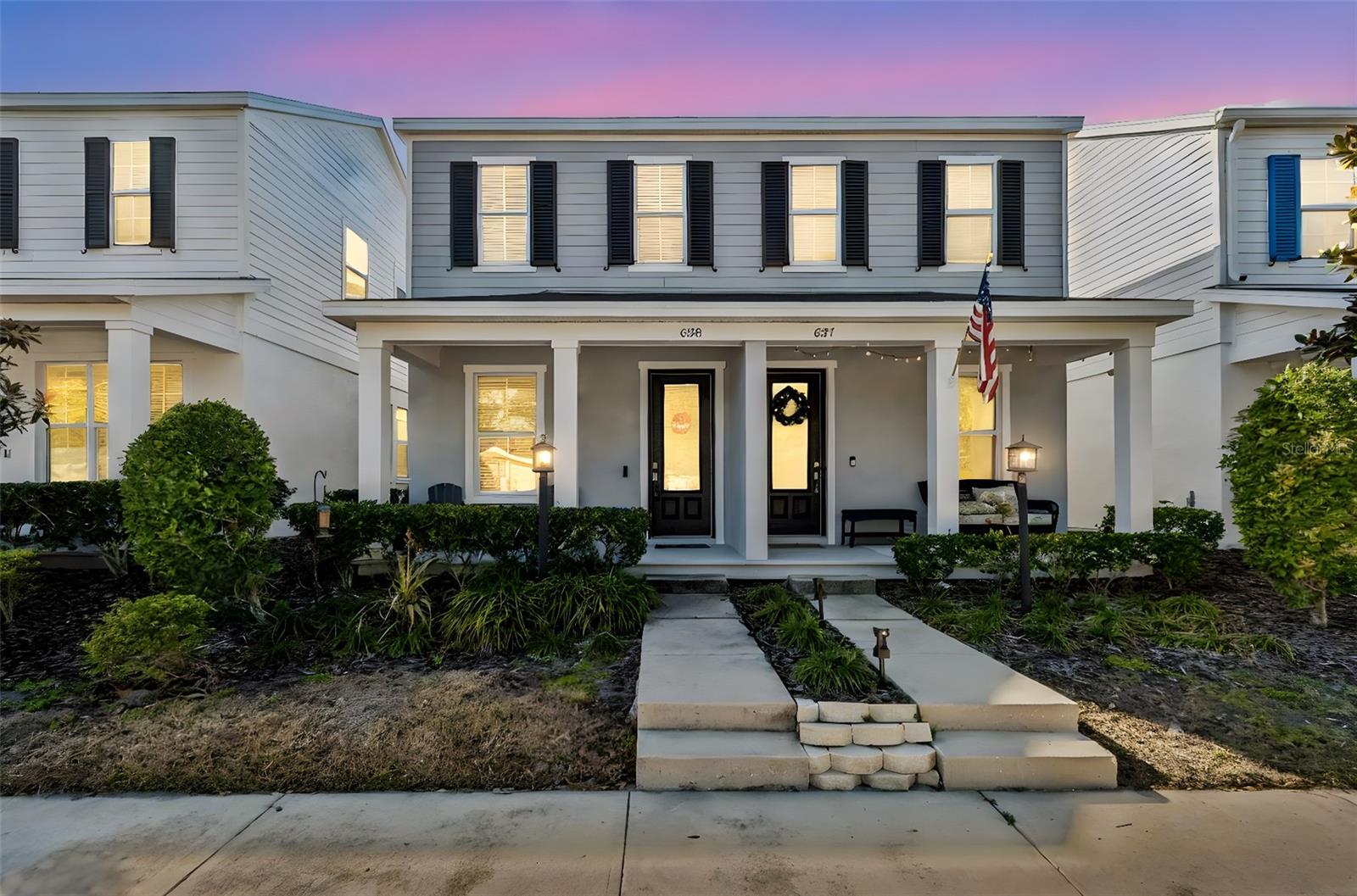 Charming two-story exterior with inviting curb appeal, highlighted by classic black shutters, a welcoming front porch, and manicured landscaping under a picturesque sunset sky.