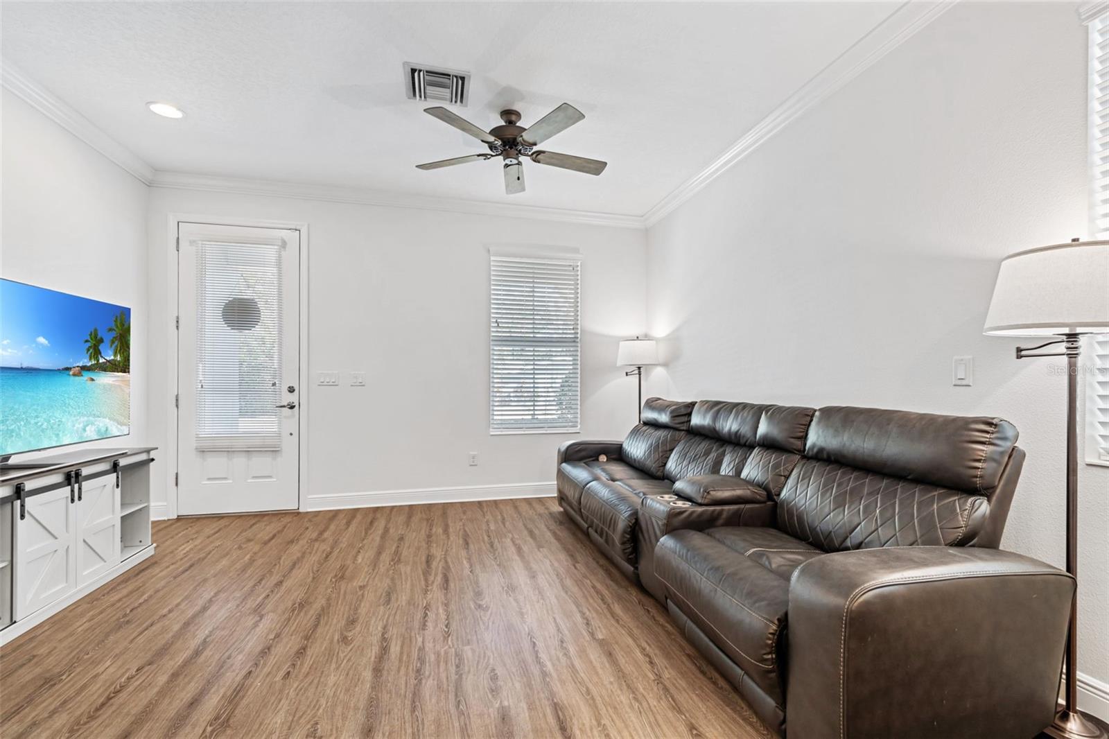 Bright and inviting living area with crown molding, recessed lighting, and a sleek ceiling fan—offering seamless access to the front door and side patio.