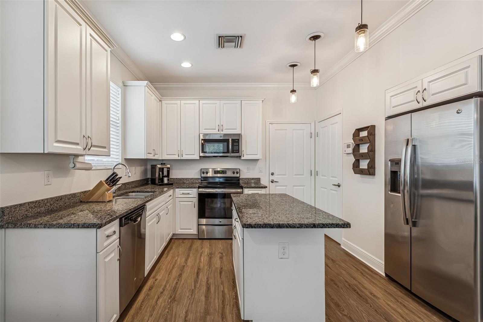 This updated kitchen features granite countertops, white cabinetry, and stainless steel appliances, including a built-in microwave and electric range.
