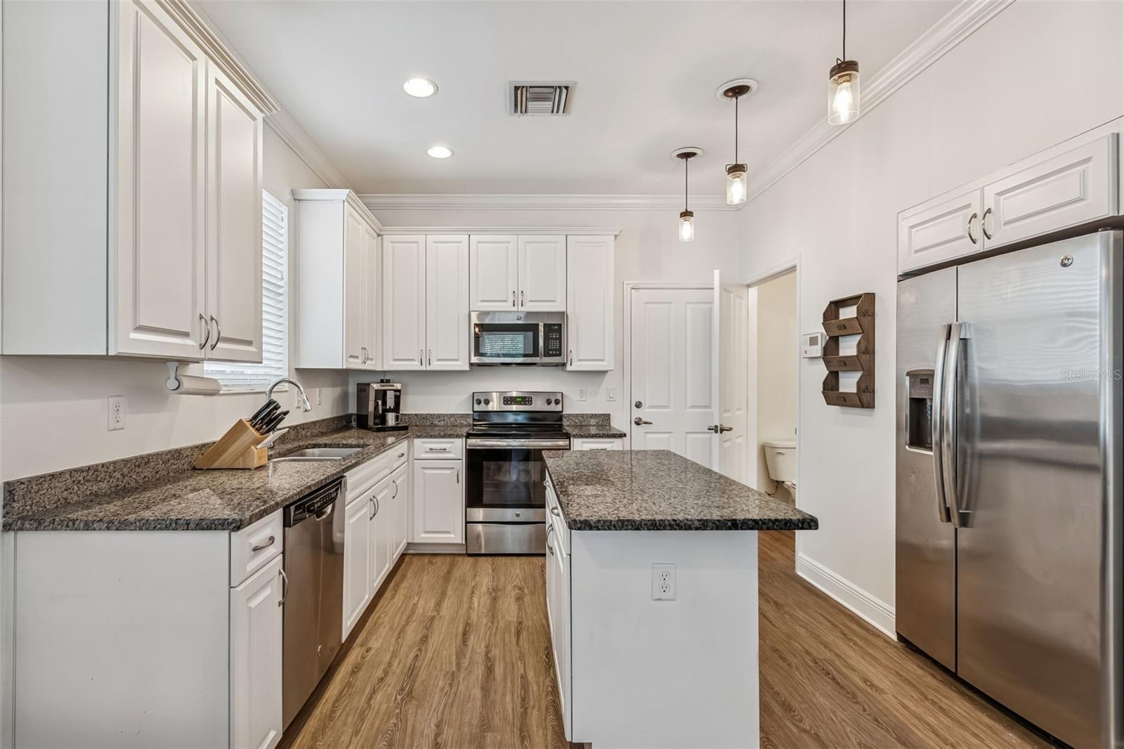 Central island adds prep space and seating potential, surrounded by extensive cabinetry and pendant lighting above.