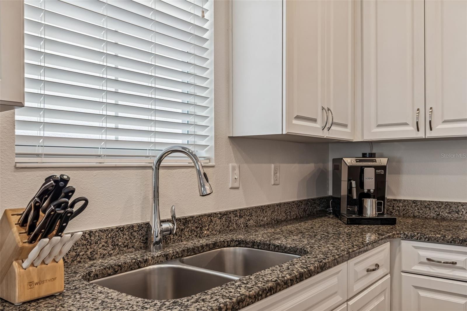 Double-basin stainless sink with pull-down faucet sits below a large window, offering a pleasant view while prepping or cleaning.
